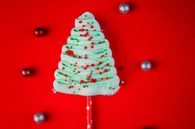 Turquoise christmas tree made of bizet on sticks strewn with colorful powder balls on a bright red b...