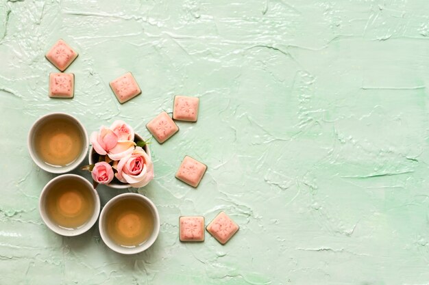 Turquoise cups with rose tea, rose blossoms, pink chocolate on neo mint