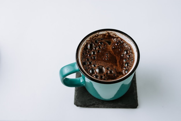 Turquoise enamel mug with black coffee on black coaster.