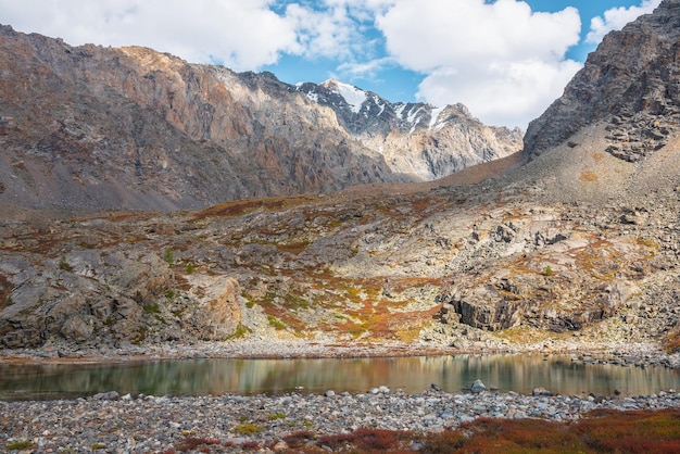 写真 秋の多色の植物のなかで青い山の山の湖青い空の雲の下の太陽の光に照らされた高い岩の山頂の岩の上に日光に照らされたアルプス湖と大きな山脈鮮やかな秋の色