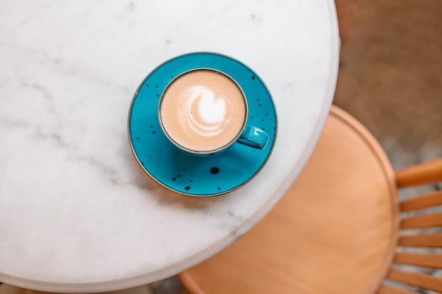 Turquoise mug of flat white coffee with heart shaped latte art on white table at the hipster coffee shop Flat lay copy space