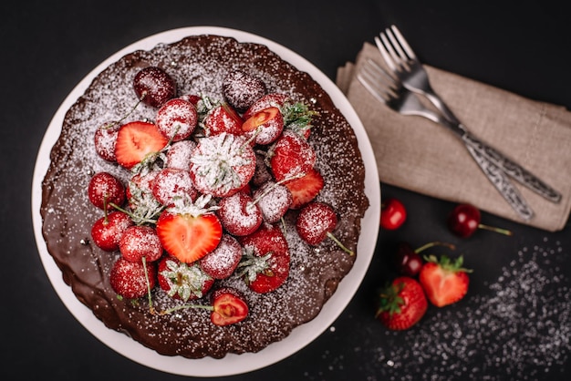 Tuscan chocolate cake with strawberries and cherries on dark background