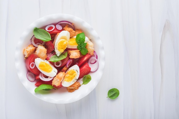 Tuscan panzanella salad fresh tomatoes salad with basil leaves\
eggs olive oil and onion in white bowl on light background\
vegetarian panzanella salad mediterranean healthy food top\
view