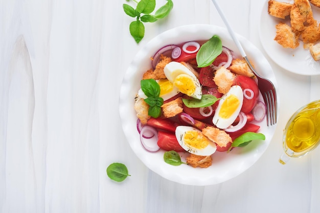 Tuscan panzanella salad fresh tomatoes salad with basil leaves\
eggs olive oil and onion in white bowl on light background\
vegetarian panzanella salad mediterranean healthy food top\
view