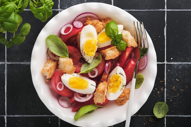 Tuscan panzanella salad fresh tomatoes salad with basil leaves\
eggs olive oil and onion in white bowl on old black background\
vegetarian panzanella salad mediterranean healthy food top\
view