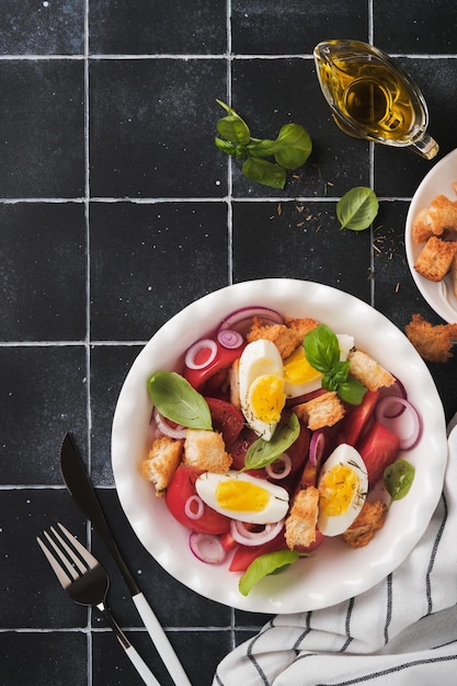 Tuscan Panzanella salad Fresh tomatoes salad with basil leaves eggs olive oil and onion in white bowl on old black background Vegetarian panzanella salad Mediterranean healthy food Top view