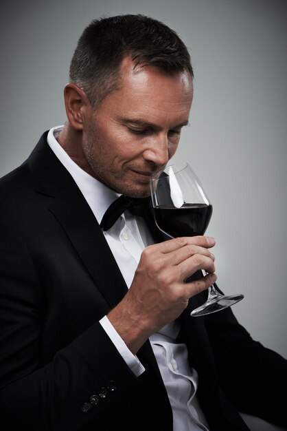 Tuxedo wine glass and man with alcohol in a suit feeling classy with a luxury drink Gray background isolated and studio with a model agent or actor with a glass to smell rich wines with mockup