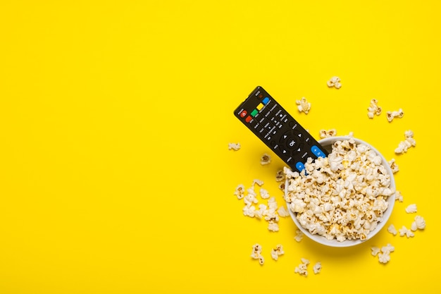 TV remote control, TV tuner lie in a bowl with popcorn on yellow