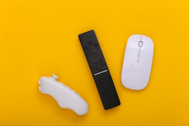 Tv remote, joystick, pc mouse on yellow background.
entertainment and gadgets. top view