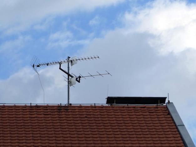 Телевизионная спутниковая тарелка и антенны на крыше дома на фоне облачного голубого неба