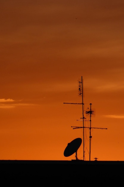 TV satellite dish and antennas on a house roof at sunset