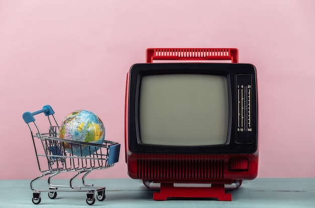 Foto tv supermarkt. winkelwagentje met globe, retro tv op roze achtergrond