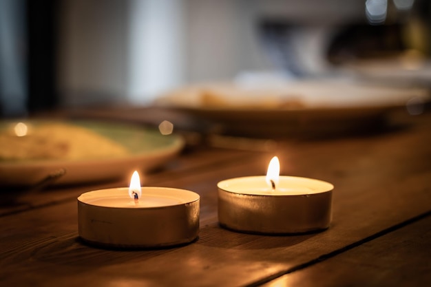 twee aangestoken kaarsen bovenop een bruine houten tafel, met plaat op de achtergrond.