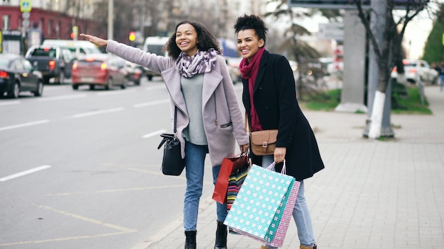 Twee aantrekkelijke Afro-Amerikaanse vrouwen met boodschappentassen die om een taxi vragen