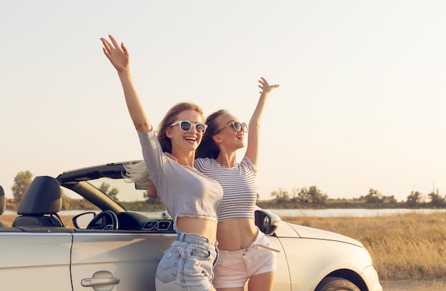 Twee aantrekkelijke jonge vrouwen in de buurt van een converteerbare auto