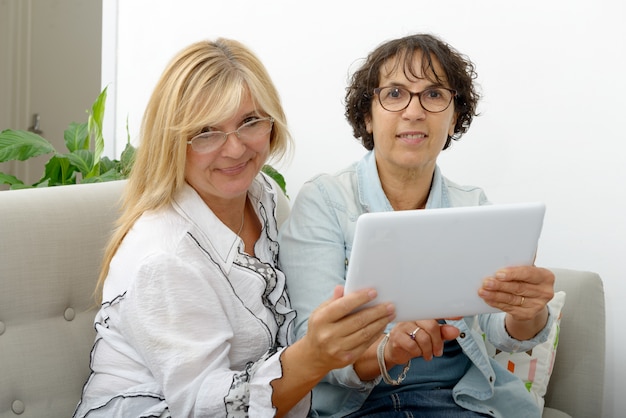 Twee aantrekkelijke rijpe vrouwen die met tablet websurfing