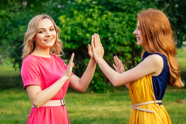 Twee actieve vrolijke vriendinnen mooie jonge gember roodharige Ierse meisje in een gele jurk en Europese blonde vrouw in een roze jurk spelen in het zomerpark. twee vriendinnen ontmoeten