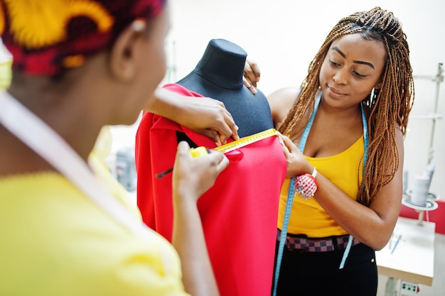 Twee Afrikaanse naaistervrouw ontwierpen nieuwe rode jurk op mannequin op kleermakerskantoor Zwarte naaistermeisjes