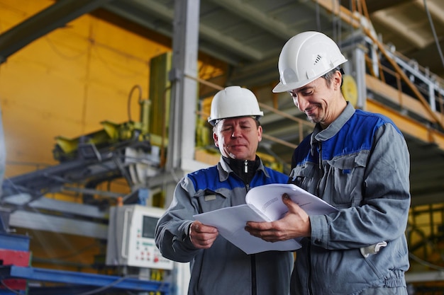 Twee arbeiders in overalls die documenten vasthouden en ernaar kijken in het fabrieksgebouw