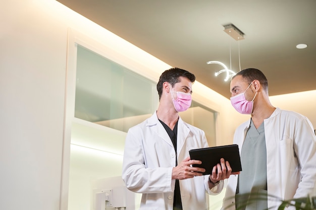 Twee artsen in een masker becommentariëren de resultaten met een tablet in de hand. Gynaecologische, tandheelkundige of esthetische kliniek. Medisch concept.