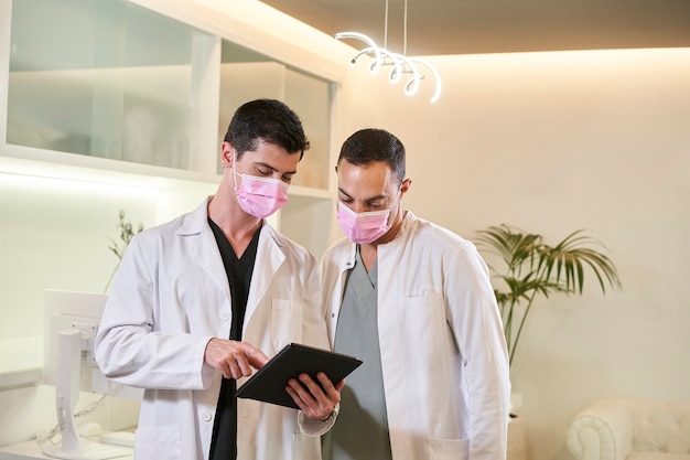 Twee artsen met maskers kijken naar het tabletscherm in een gynaecologische, tandheelkundige of esthetische kliniek.