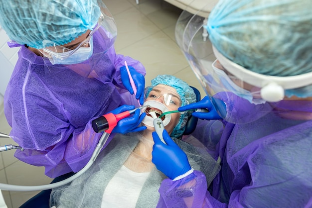 Twee assistenten van de tandarts in speciale kleding in handschoenen en maskers helpen de tandarts om de probleemtand van de patiënt te opereren Het concept van chirurgie in de tandheelkunde