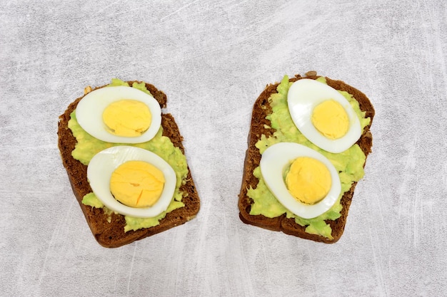 Twee avocadosandwiches met hardgekookte eieren bovenop geïsoleerd op grijze achtergrond