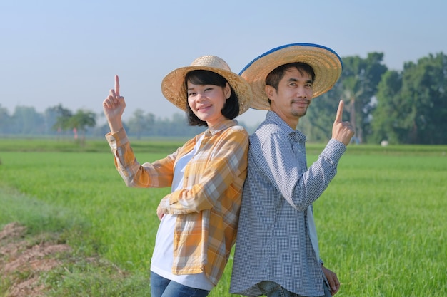 Twee Aziatische boeren poseren met hun vingers naar de top voor presentatie op een groene rijstboerderij. Paar boeren concept.