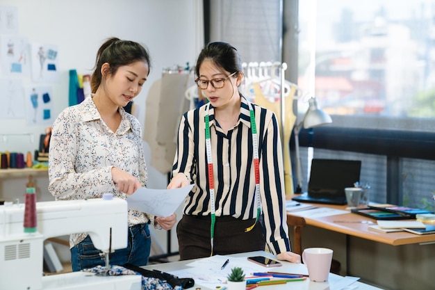 Twee Aziatische Japanse vrouwelijke modeontwerper collega's creatieven bespreken tijdschriftlay-out op kantoor. werkende partners wijzen en praten over plan op papierwerk met nieuwe seizoenskleding in studio.