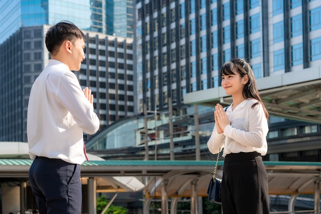 Twee Aziatische jonge zakenman en zakenvrouw vrienden ontmoeten elkaar in lettertype van kantoorgebouw In plaats van te begroeten met een knuffel of handdruk, betalen ze in plaats daarvan respect.