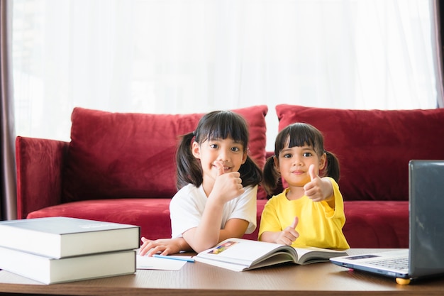 Twee aziatische kindmeisjesstudenten studeren samen online met de leraar door middel van een videogesprek.
