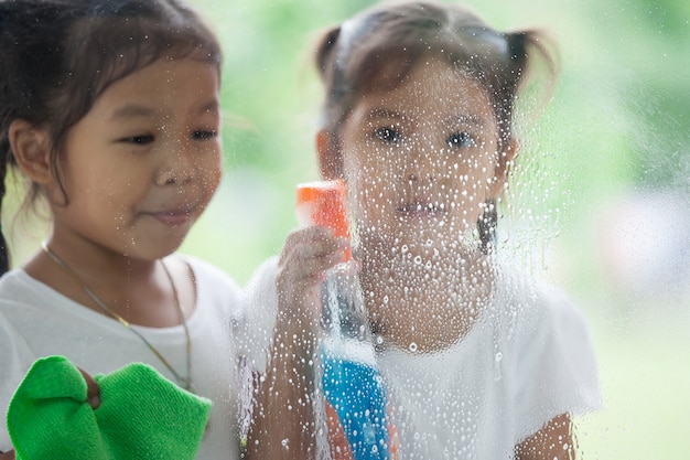 Twee Aziatische kleine kindmeisjes die pret hebben om ouder te helpen om venster samen schoon te maken