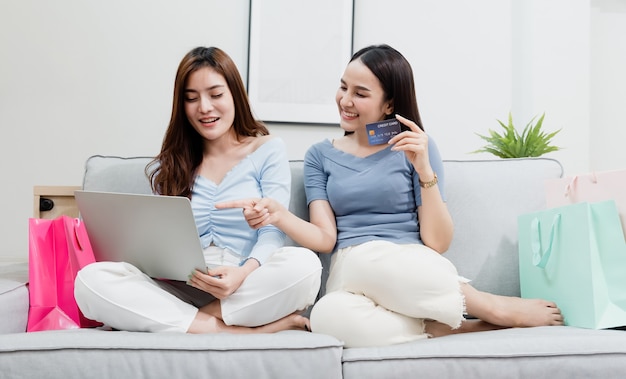 Foto twee aziatische schoonheidsmensen gebruiken een creditcard om via internet aankopen te doen met een laptop. met een blij lachend gezicht, een nieuw normaal online bedrijf zijn in de winkelervaring vanuit huis