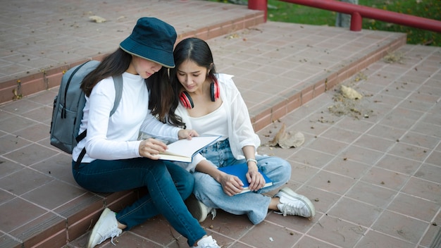 Twee aziatische studenten delen notities terwijl ze op de trap op de universiteitscampus zitten.