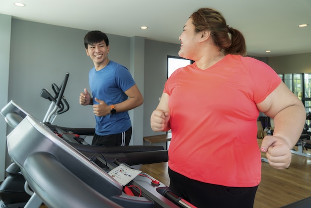 Twee aziatische trainer man en overgewicht vrouw trainen op de loopband in de sportschool, trainer bonzen omhoog