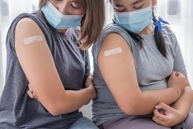 Twee Aziatische vrouwen dragen een masker en kijken naar de arm nadat ze een vaccin covid hebben gekregen