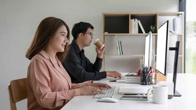 Twee Aziatische zakenmensen zitten samen in een modern kantoor en werken met de computer.