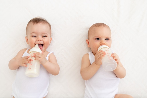 Twee baby's zuigen melk uit een fles die in een wiegje in de kinderkamer op een wit bed ligt