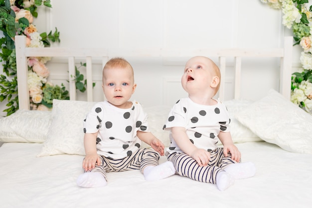 Twee baby-tweeling 8 maanden oud zittend op het bed in dezelfde kleding, broer-zus relatie, modieuze kleding voor kinderen van een tweeling