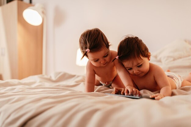 Twee babymeisjes die op bed met mobiele telefoon liggen