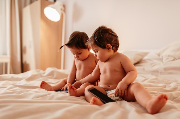 Twee babymeisjes die op bed met mobiele telefoon liggen