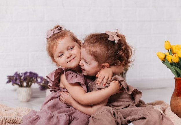 Twee babymeisjes knuffelen en glimlachen in een kamer met bloemen