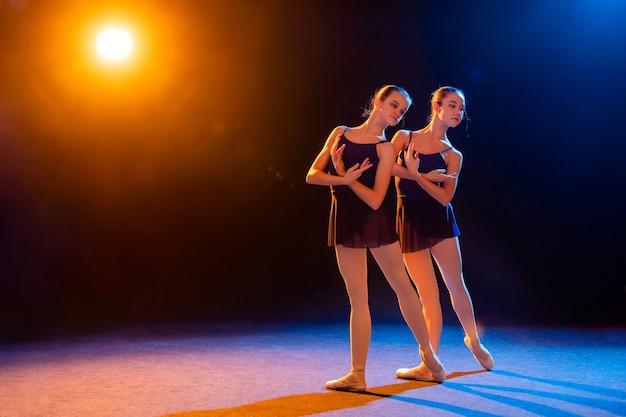 Twee ballerina's in zwarte jurk poseren verlicht door veelkleurige stralen van schijnwerpers