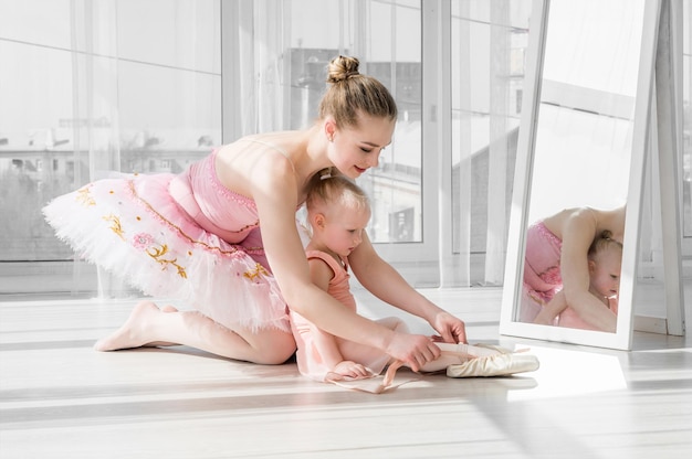 Twee ballerinas moeder en dochter zitten op het touw voor grote ramen in de studio kleine ballerina meisje en haar leraar doen de split klein meisje strekken met haar moeder