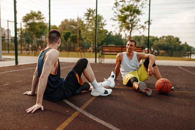 Twee basketbalspelers zittend op de grond op buitenhof