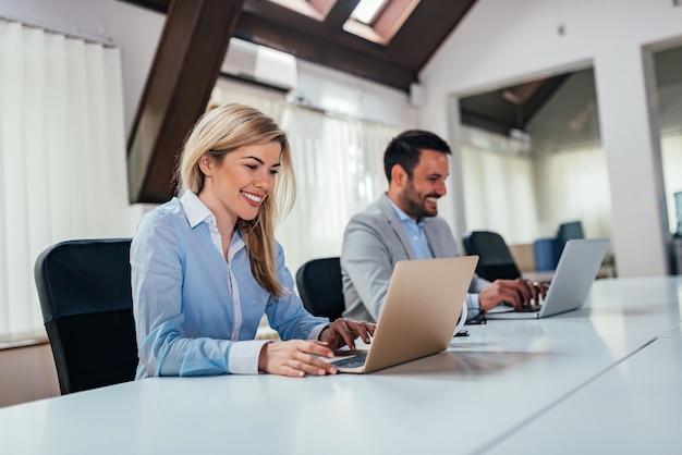 Twee bedrijfsmensen die aan laptops bij open kantoorruimte werken.