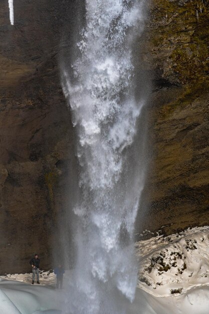 Twee bergsporttoeristen achter de bevroren Kvernufoss-waterval met sneeuw en stalagmieten