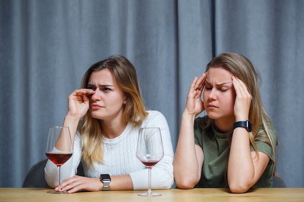 Twee beste vrienden. Jonge Europees ogende vrouwen praten aan een bureau met een glas wijn in de hand. mooie meisjes zussen houden van alcohol drinken lachen vrolijk ontspannen in de woonkamer