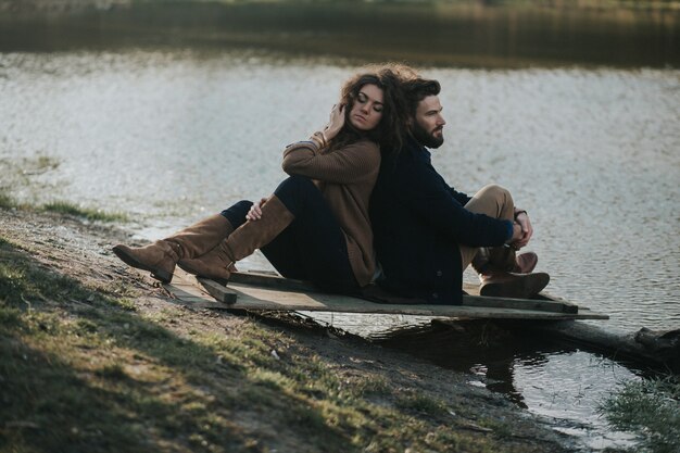 Twee blanke geliefden zittend op de pier bij het meer. Een bebaarde man en een gekrulde vrouw verliefd. Valentijnsdag.