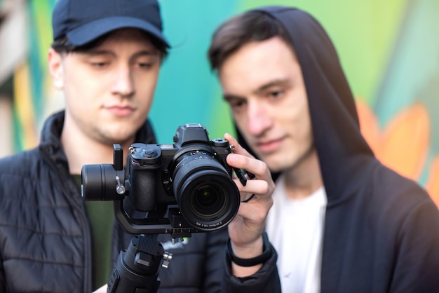 Twee blanke mannen op zoek naar het camerascherm op een steadicam, gekleurde achtergrond